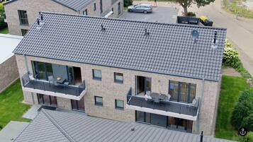 Ein mehrgeschossiges Wohngebäude mit grau gefließtem Dach, Balkonen mit Geländern und einer Satellitenschüssel.