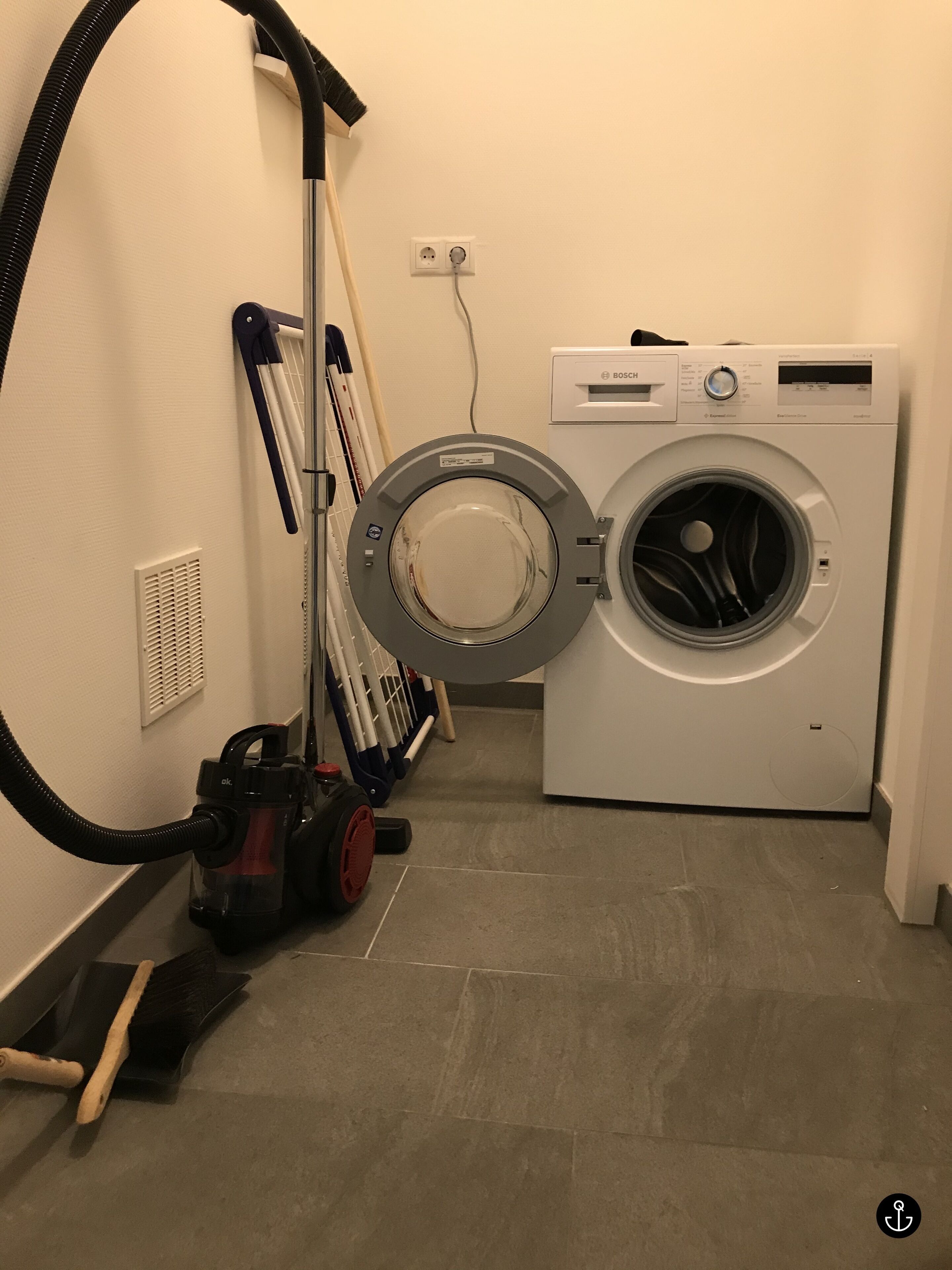 A laundry area with a Bosch washing machine, a vacuum cleaner, and a mop.