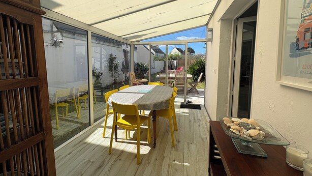 Une terrasse couverte avec une table et des chaises, une vitrine contenant des coquillages et un tableau encadré accroché au mur.