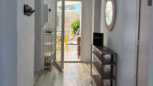 Un couloir avec une lucarne, une porte-fenêtre coulissante donnant sur un espace extérieur, une étagère en métal et un miroir rond accroché au mur.