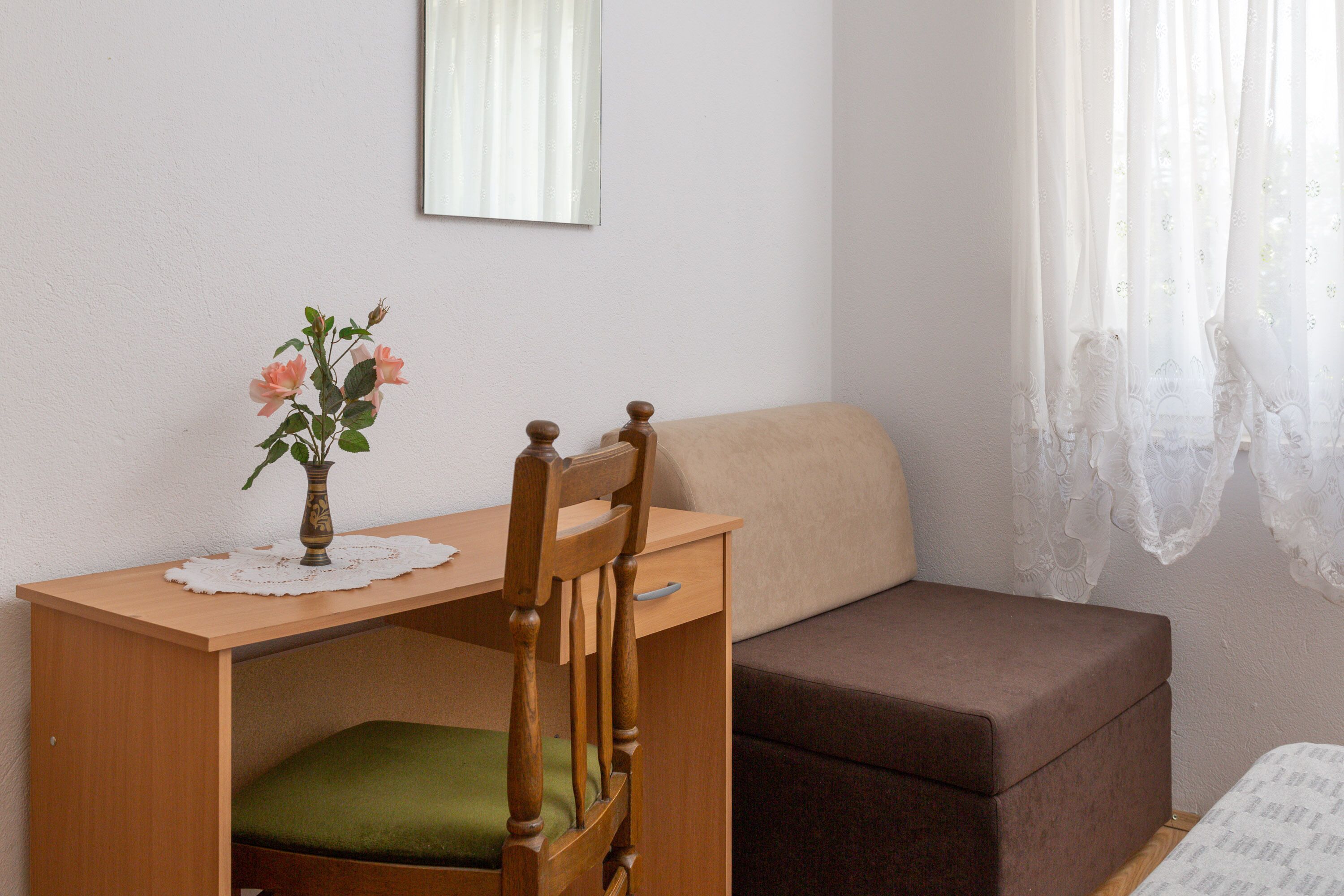 A small room with a wooden desk, a chair, a brown sofa, and a small table with a vase of flowers.