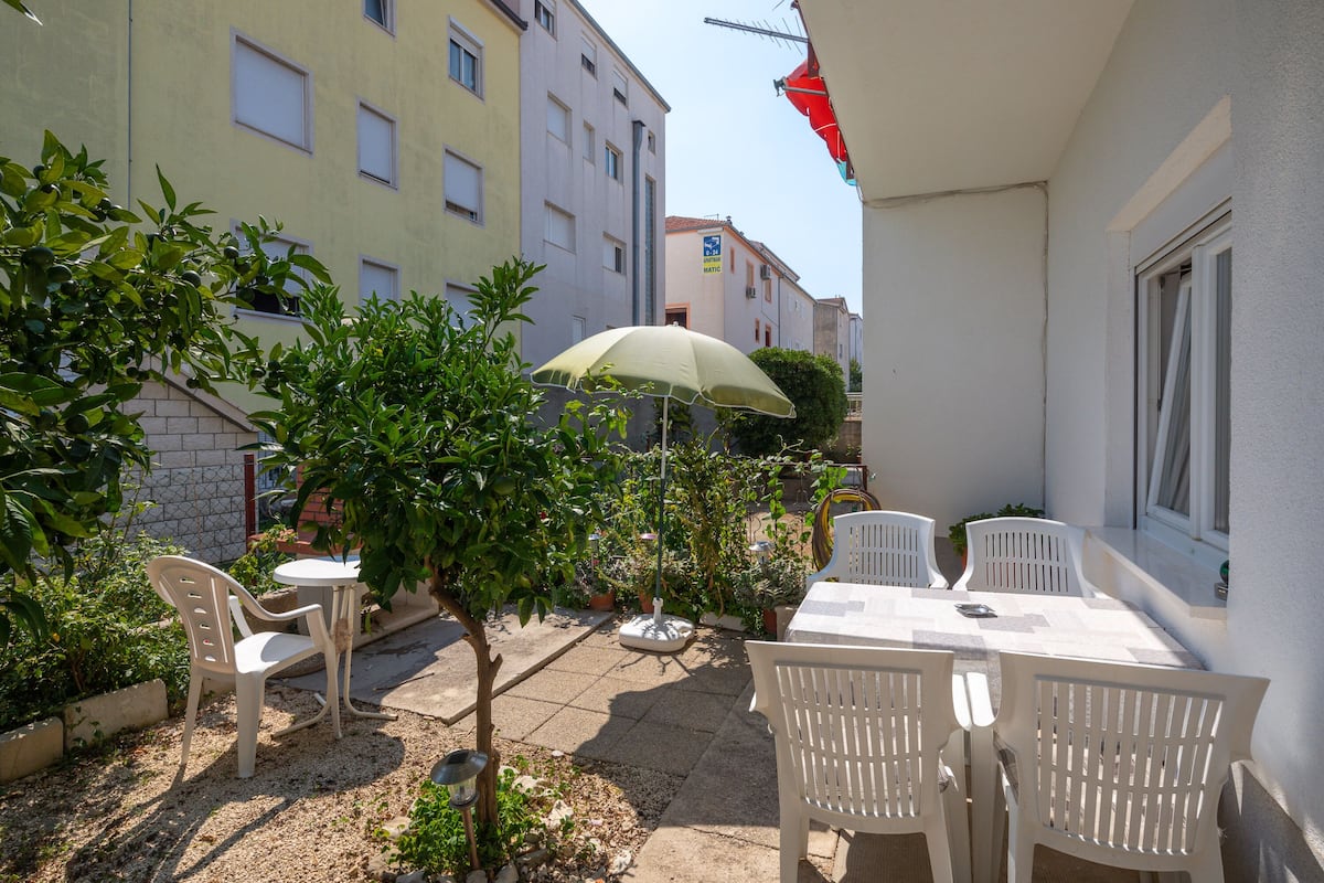 An outdoor patio with a table and chairs, surrounded by potted plants and a small tree.