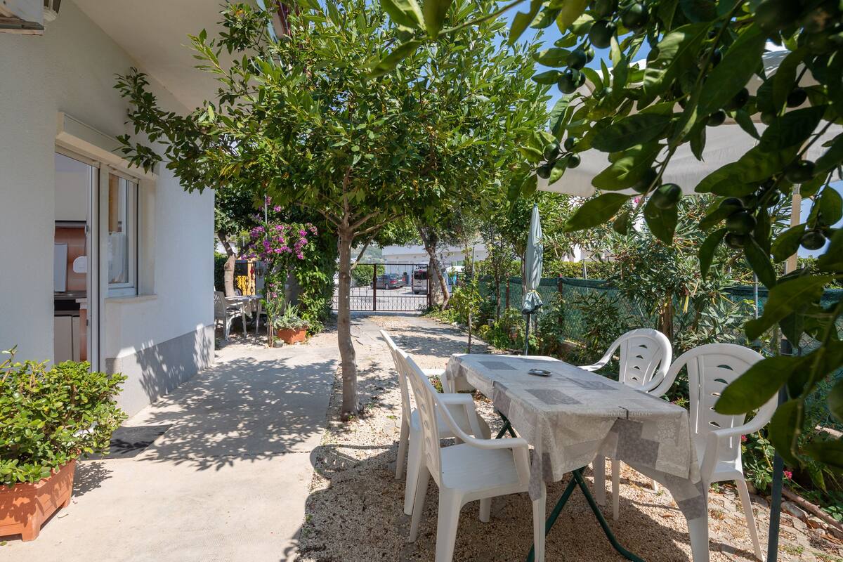 An outdoor patio with a table and chairs, surrounded by greenery and a building.