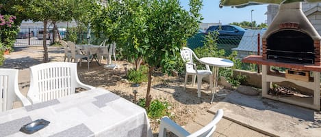 Un patio al aire libre con una mesa, sillas, un árbol pequeño y un horno de ladrillo.