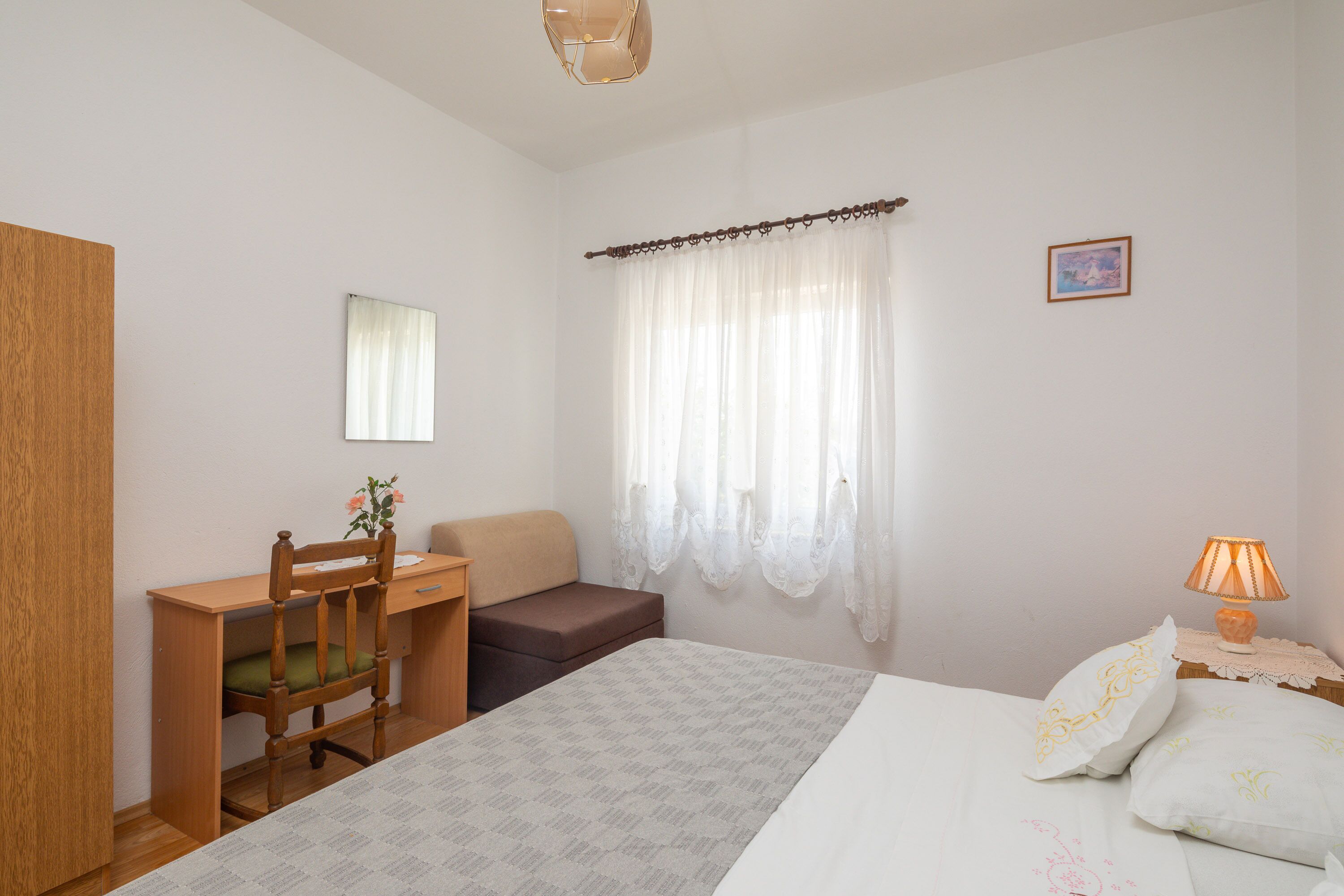 Ein Schlafzimmer mit einem Bett, einem Schreibtisch, einem Stuhl, einem Nachttisch mit Lampe und einem Fenster mit Vorhängen.