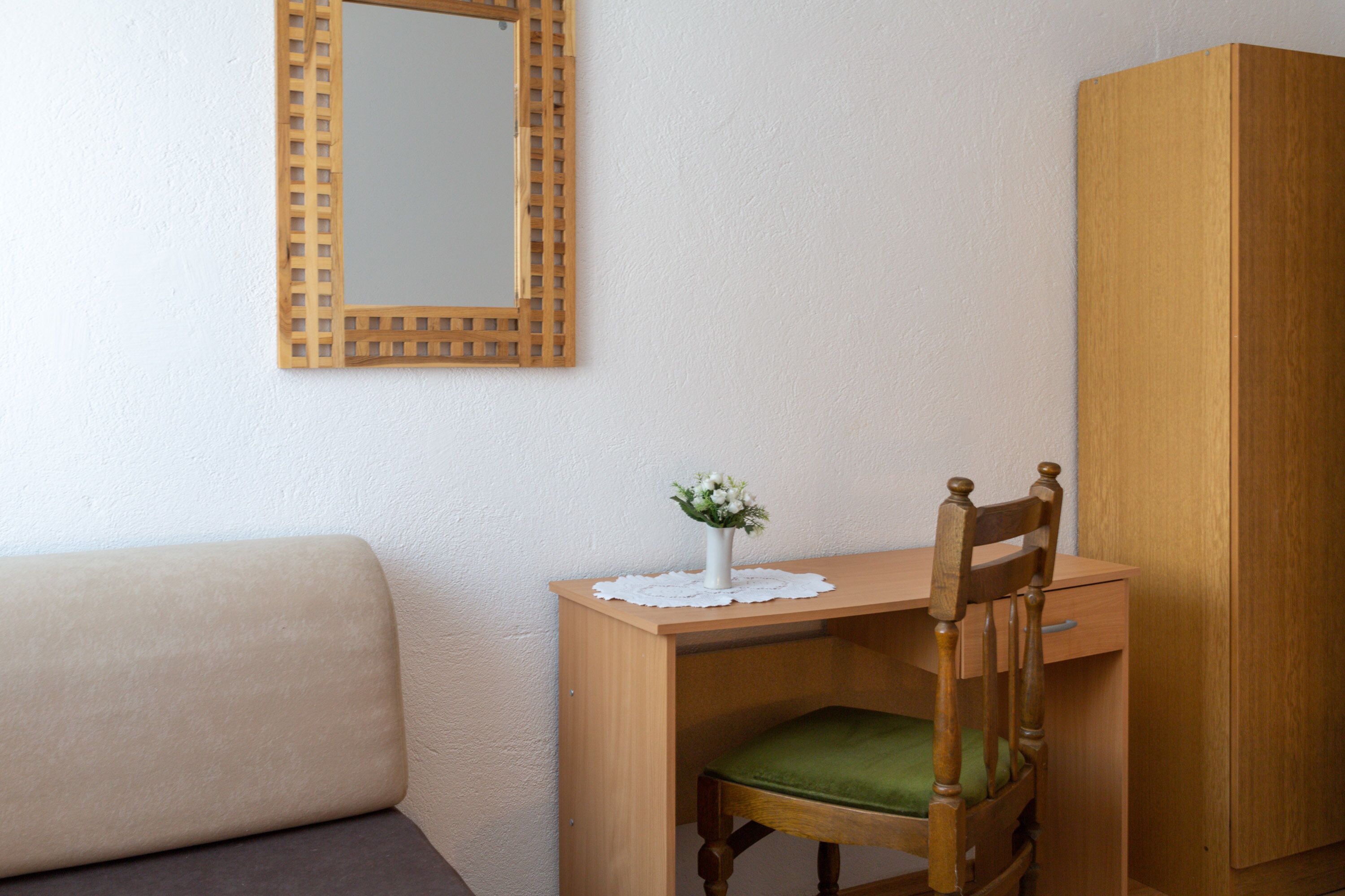 Un bureau en bois avec une chaise rembourrée verte, un vase blanc orné de fleurs et un meuble en bois adossé à un mur blanc.