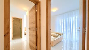 A bedroom with a bed, a wooden door, and a large window with sheer curtains.