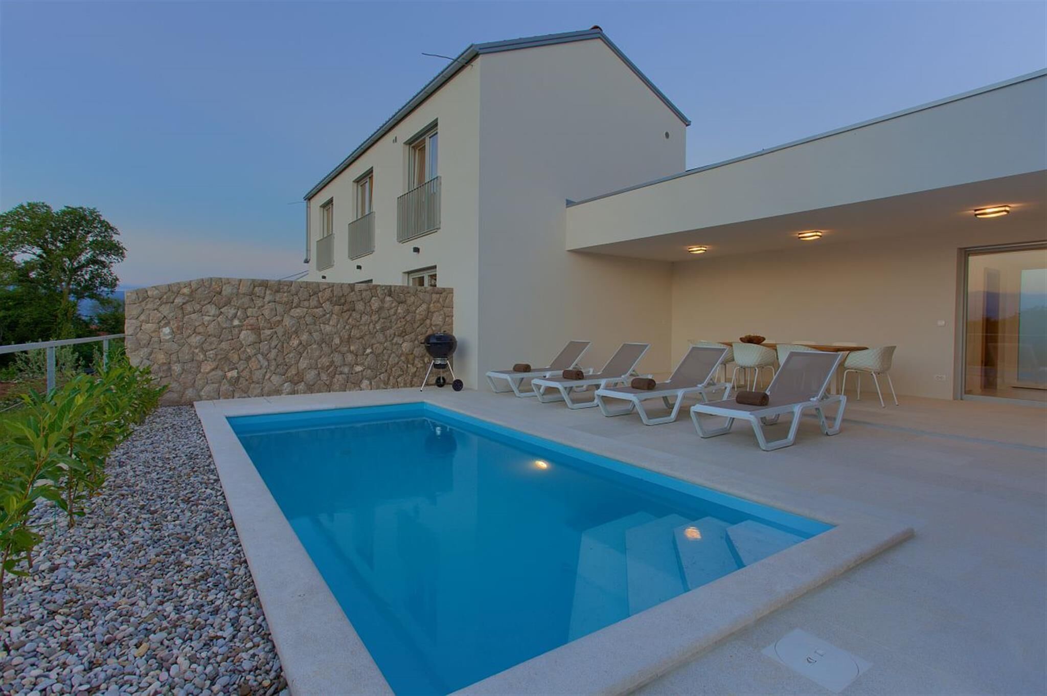A modern house with a swimming pool, lounge chairs, and a stone wall.