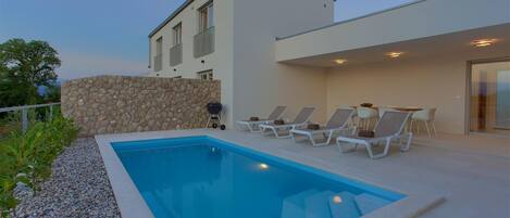 A modern house with a swimming pool, lounge chairs, and a stone wall.