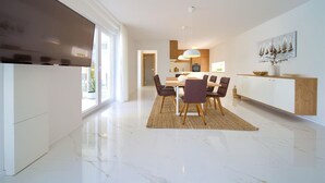 A modern kitchen with a dining area, featuring a large island, pendant lighting, and a view of the outdoors.