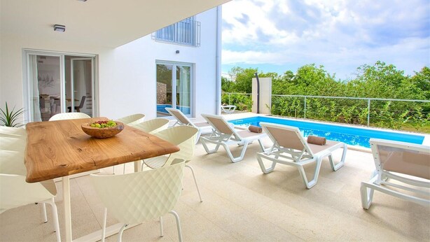 A modern outdoor patio with a wooden table, white chairs, and a pool.
