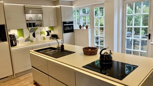 A modern kitchen with a large island, built-in appliances, and a view of the backyard through large windows. - Stylish Central House Next To Warwick Castle (Warwick)