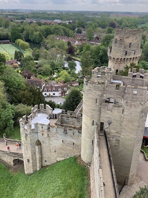 A historic castle with a moat, surrounded by lush greenery and a river.
