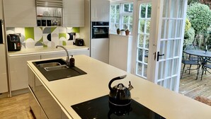 A modern kitchen with a large island, built-in appliances, and a view of the garden through glass doors. - Stylish Central House Next To Warwick Castle (Warwick)