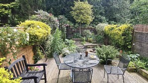 A patio with a round table and chairs, surrounded by lush greenery and a wooden fence. - Stylish Central House Next To Warwick Castle (Warwick)