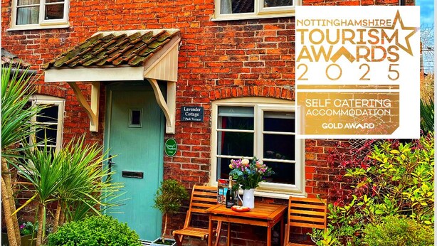 Una casa de ladrillo con una puerta azul, un cartel del Nottinghamshire Tourism Awards 2025 y una mesa con sillas afuera.