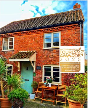 A brick house with a blue door, a sign for Nottinghamshire Tourism Awards 2025, and a table with chairs outside.