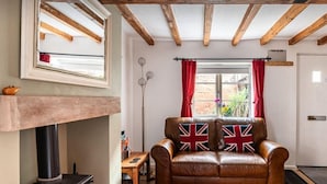Un salón acogedor con un sofá de cuero decorado con cojines con la bandera del Reino Unido, una chimenea y un techo de madera.