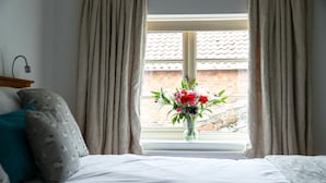 Un dormitorio con una cama, una ventana con cortinas y un florero con flores.