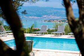 Ein Pool mit drei Liegestühlen und Blick auf eine Küstenstadt.
