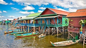 Une rangée de maisons sur pilotis donnant sur l’eau, des bateaux en bois et un ciel dégagé.