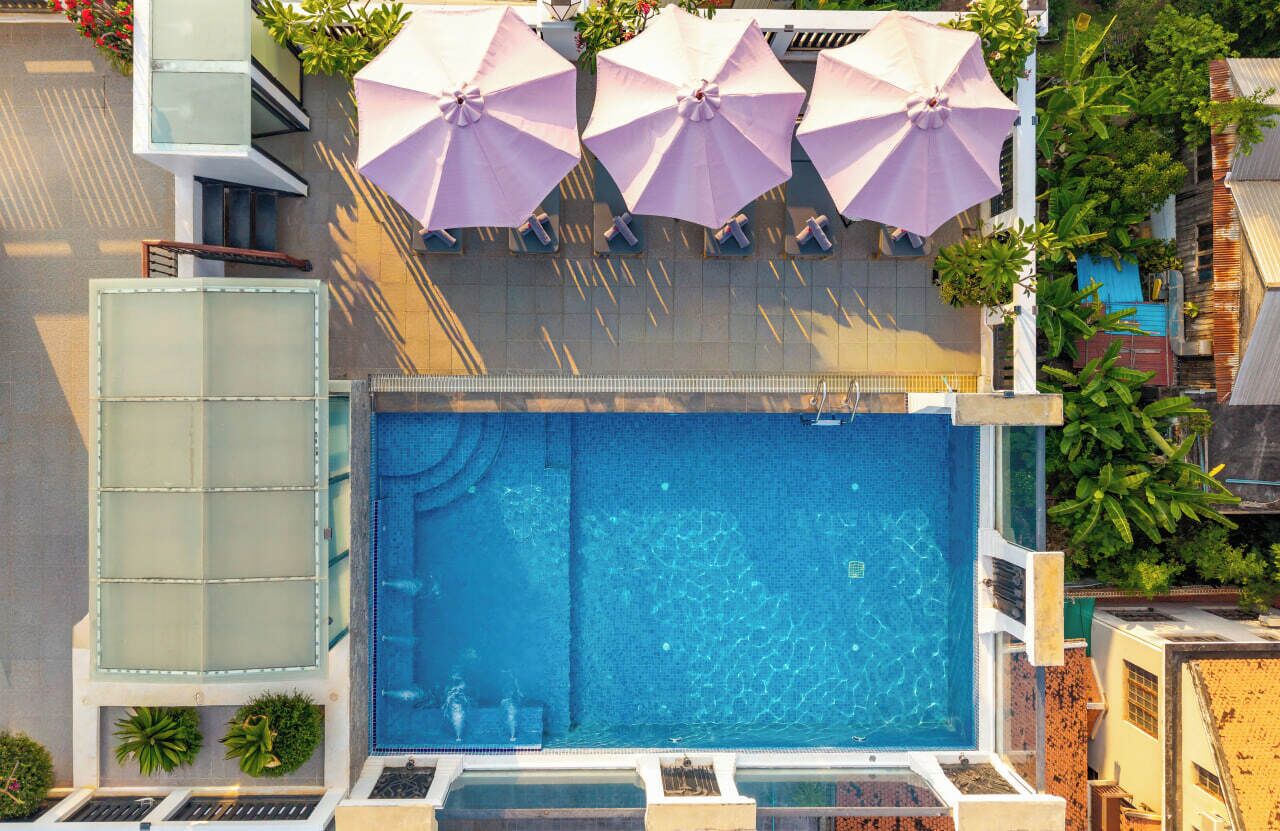 An outdoor swimming pool with a glass enclosure, surrounded by potted plants and umbrellas.