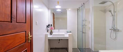A bathroom with a wooden door, a sink, a mirror, a shower, and a glass-enclosed shower area.