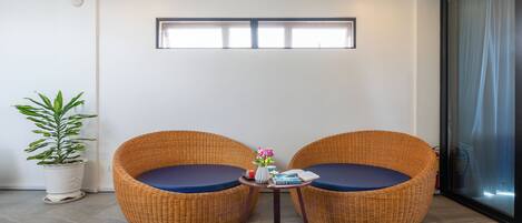 A room with two wicker chairs, a small table with a vase, and a potted plant.