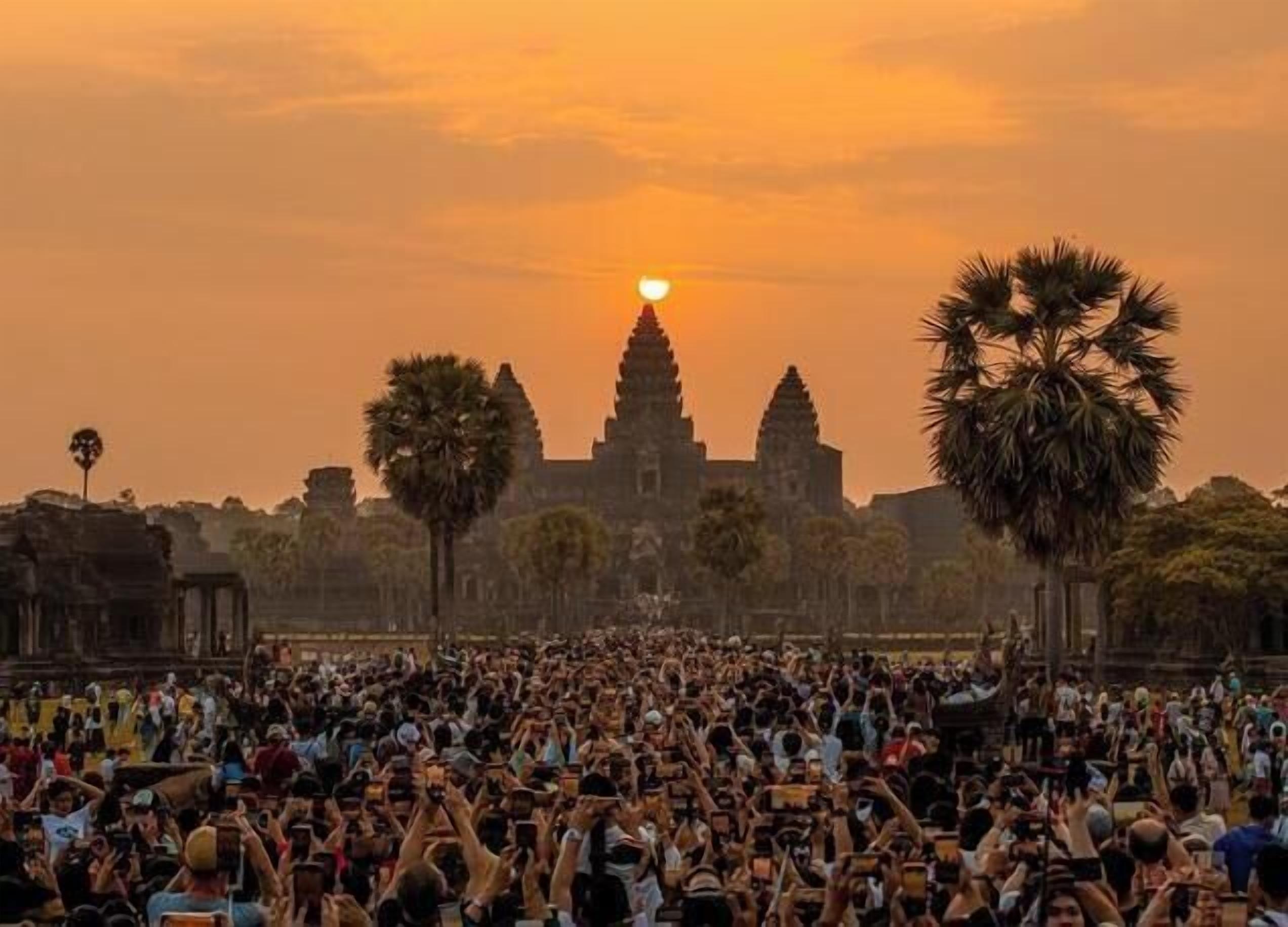 A large crowd of people in front of a historic temple with a sunset in the background.