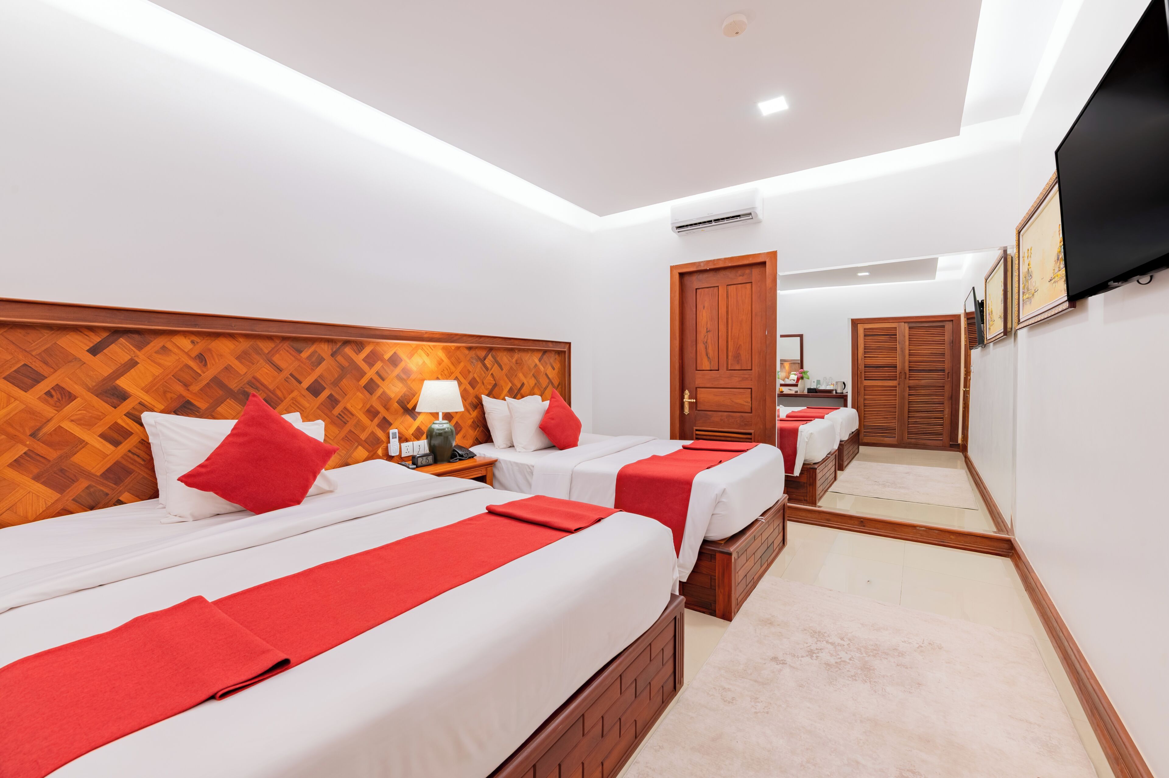 A hotel room with three beds, a TV, and a wooden headboard.