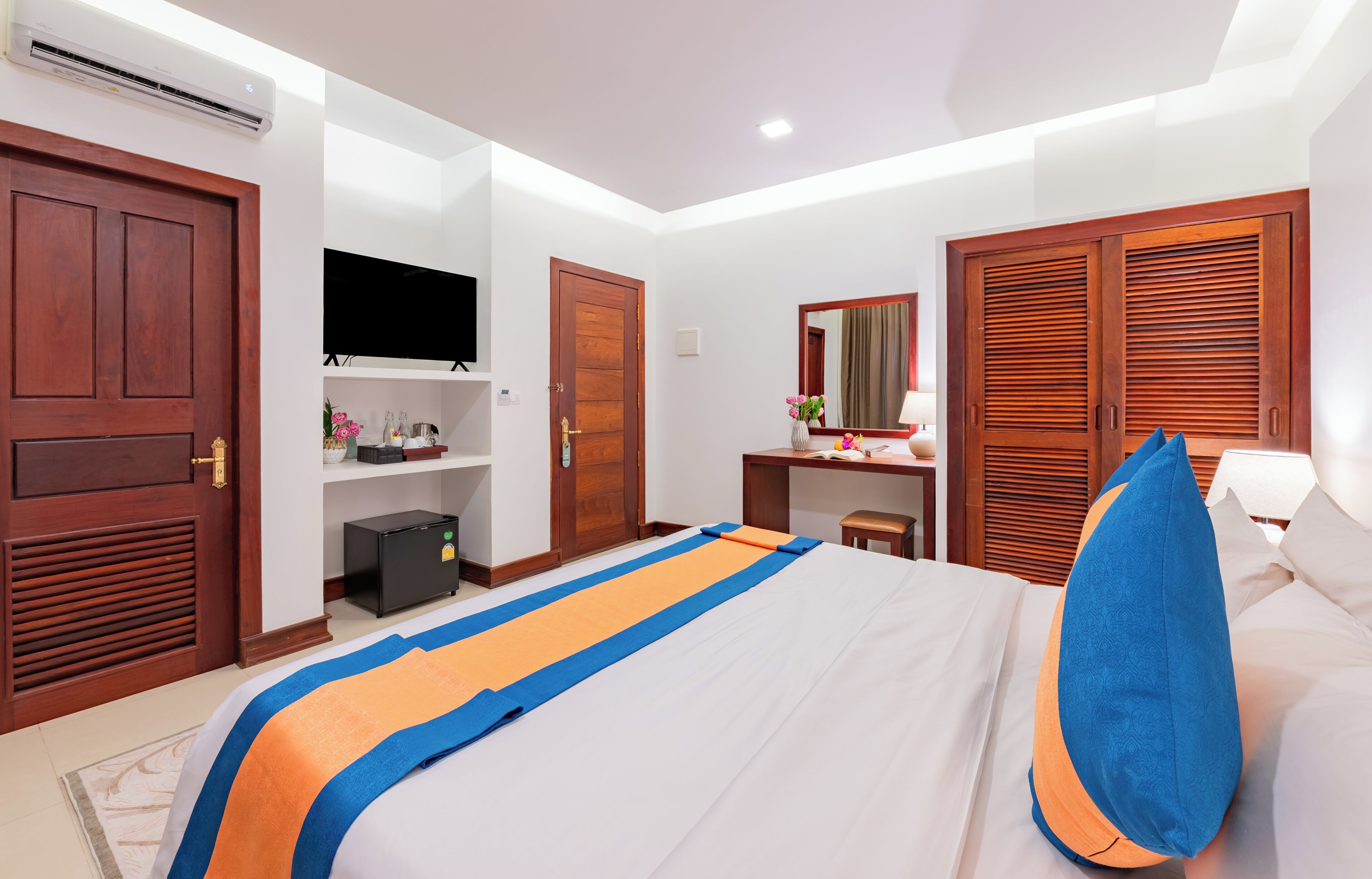 Une chambre d’hôtel équipée d’un lit, d’un bureau, d’une télévision, d’une armoire et d’un miroir.