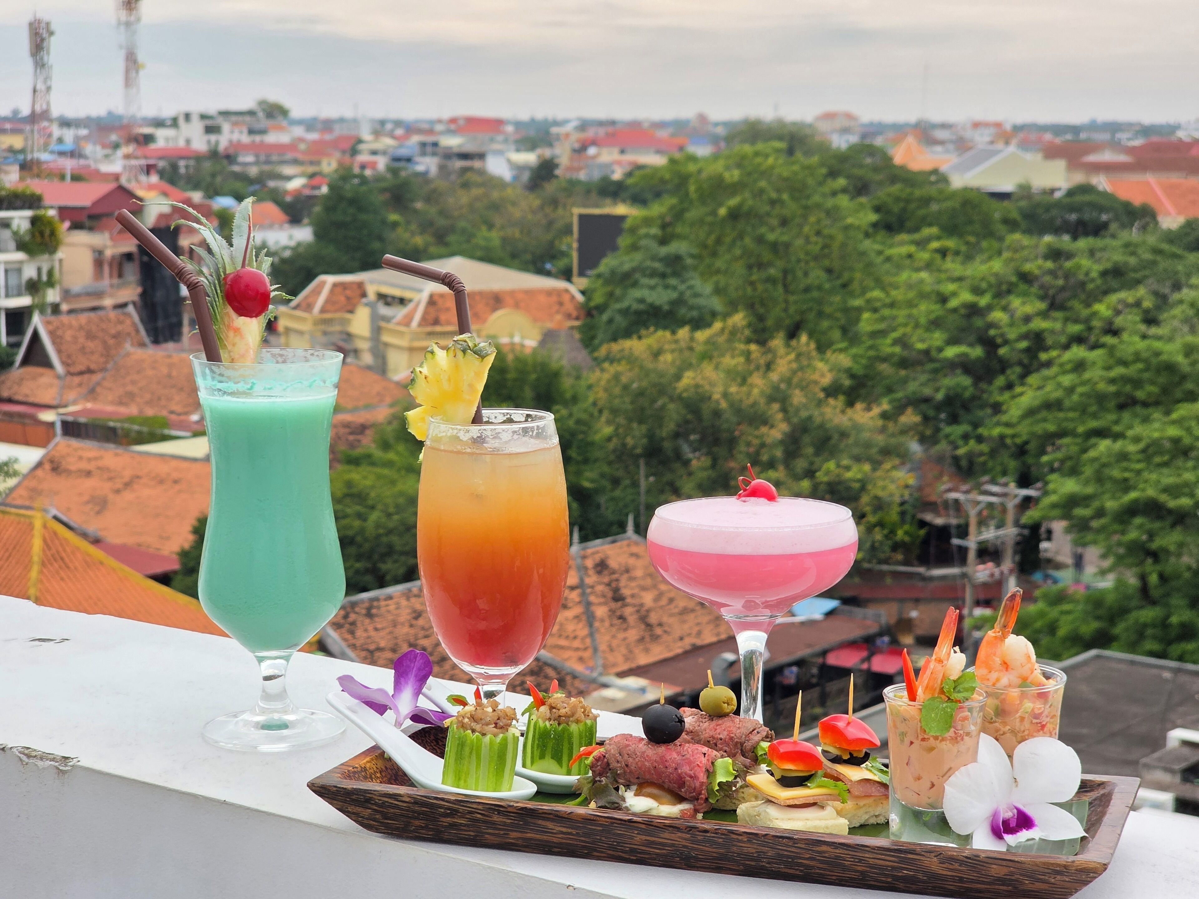 A tray of drinks and appetizers on a balcony with a cityscape view.