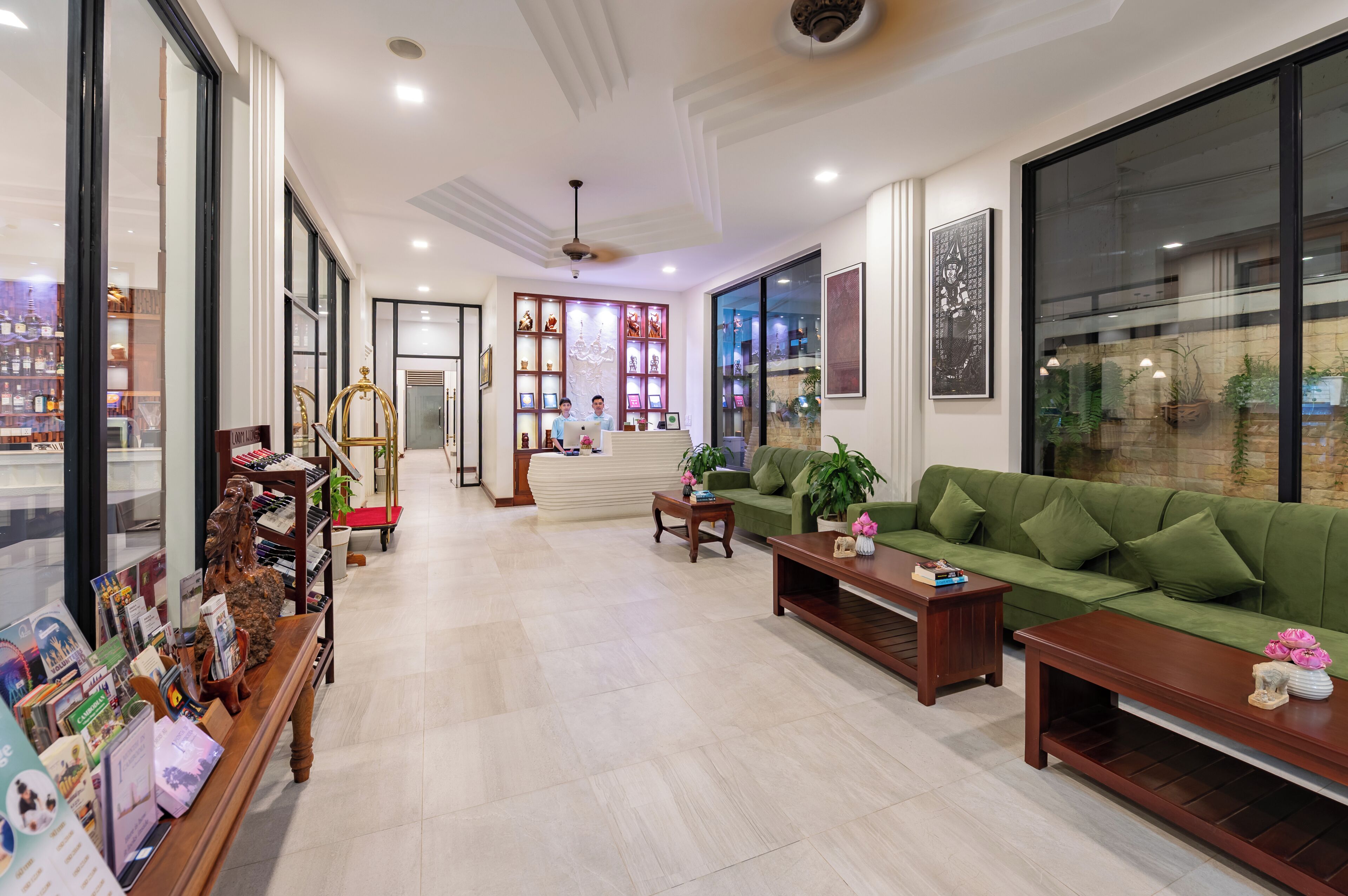 Amplia zona de estar con sofá verde, mesa de centro de madera y mostrador de recepción con exhibición de objetos.