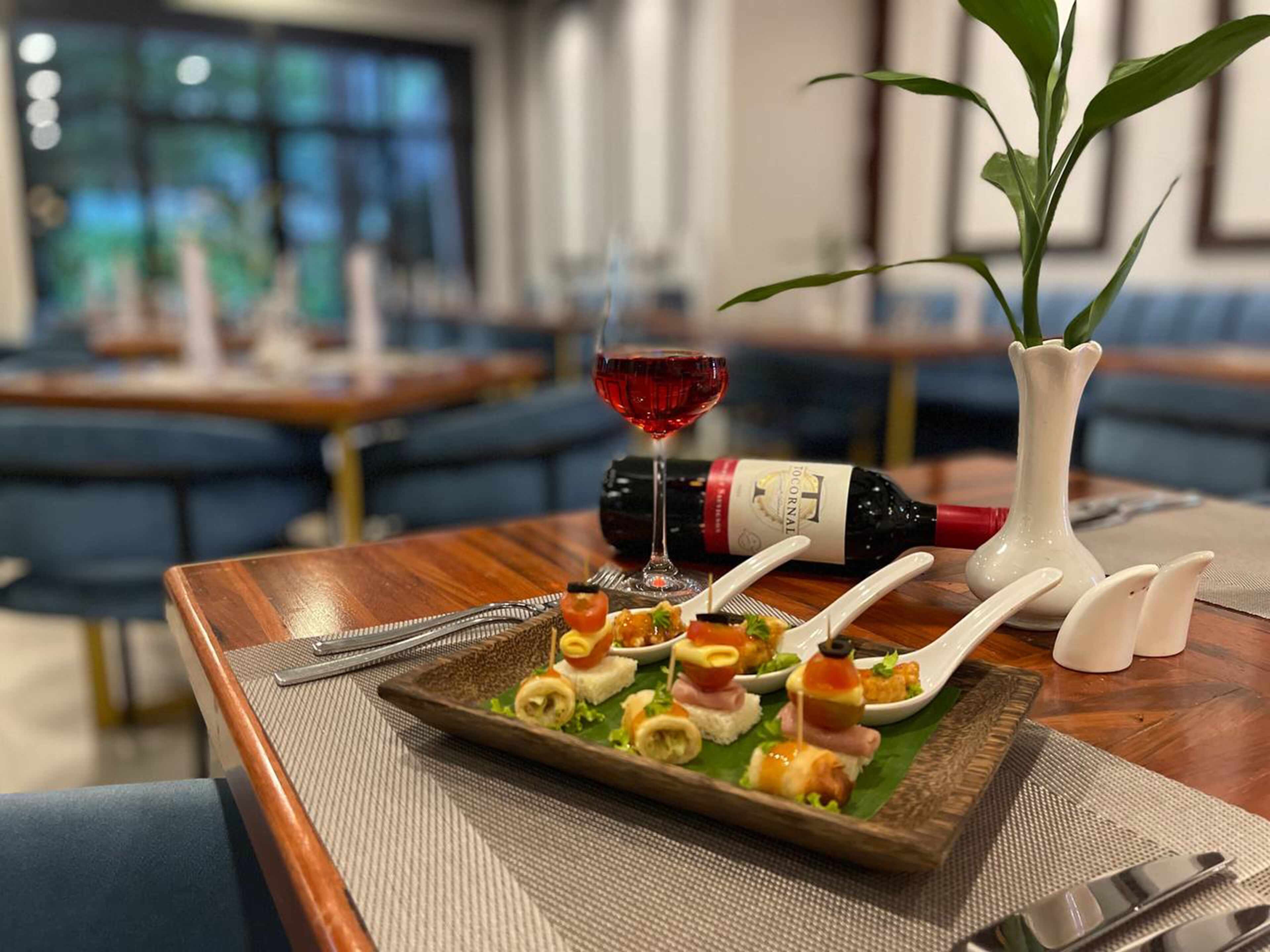 Et spisebord med en tallerken med appetizers, en vinflaske og et glas rødvin.