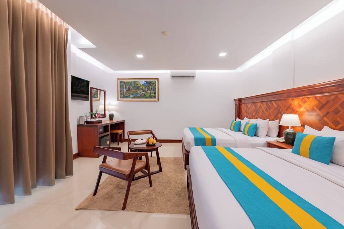 A hotel room with two beds, a desk, a chair, a TV, and a painting on the wall.