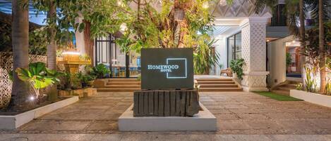 Entrada de un hotel con un letrero que dice "Homewood Hotel", rodeada de abundante vegetación y un camino de piedra.