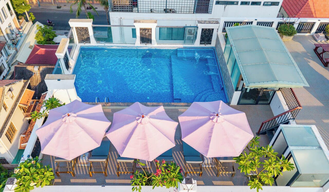 An aerial view of a hotel with a swimming pool, multiple lounge chairs, and umbrellas.