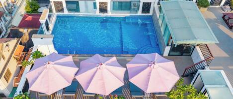 Vue aérienne d’un hôtel doté d’une piscine, de nombreuses chaises longues et de parasols.