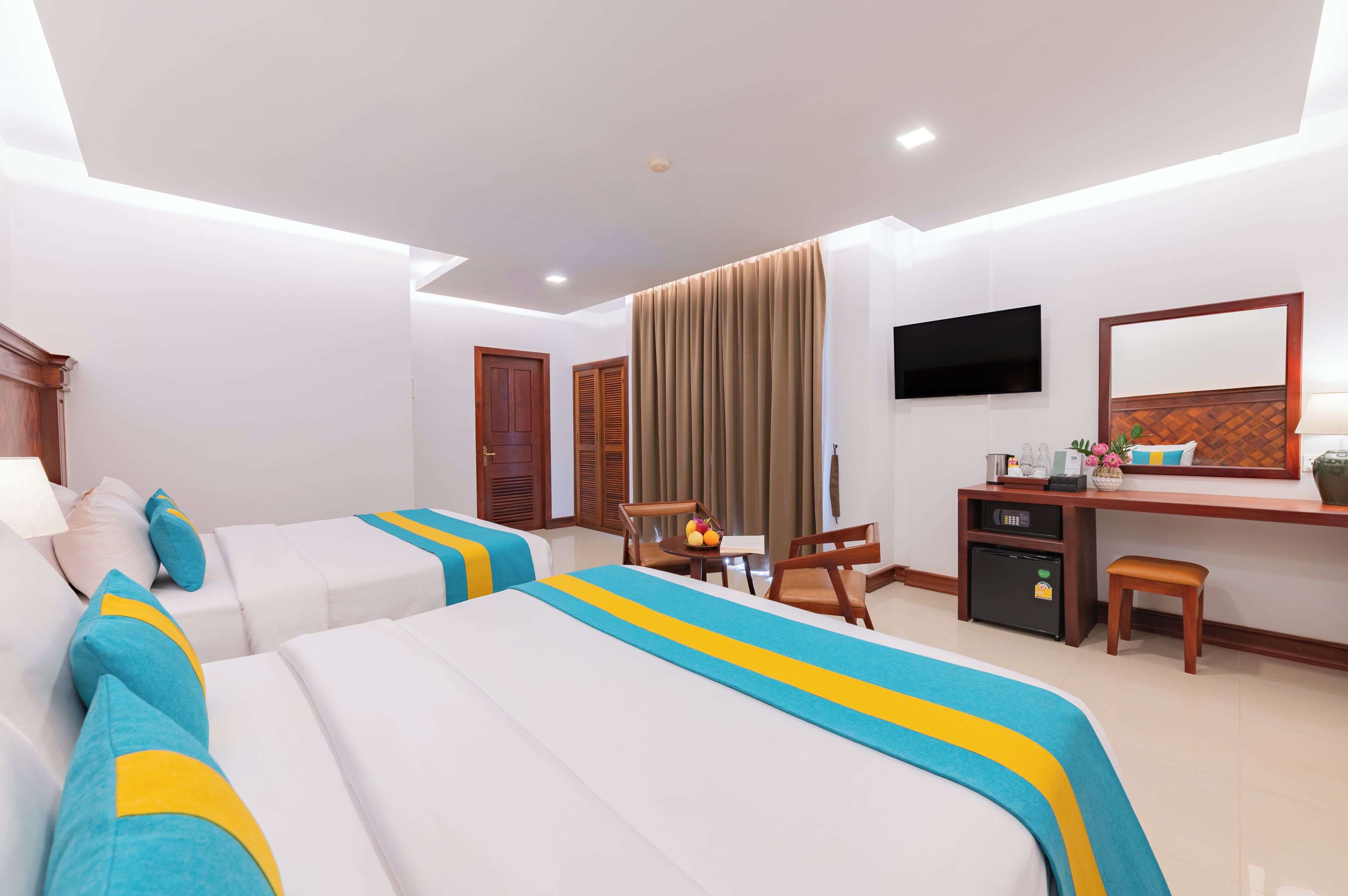 A hotel room with two beds, a desk, a chair, a TV, and a window with curtains.