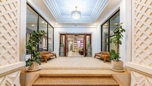 A hotel lobby with a central staircase, potted plants, and a chandelier. - Homewood Hotel (Siem Reap)