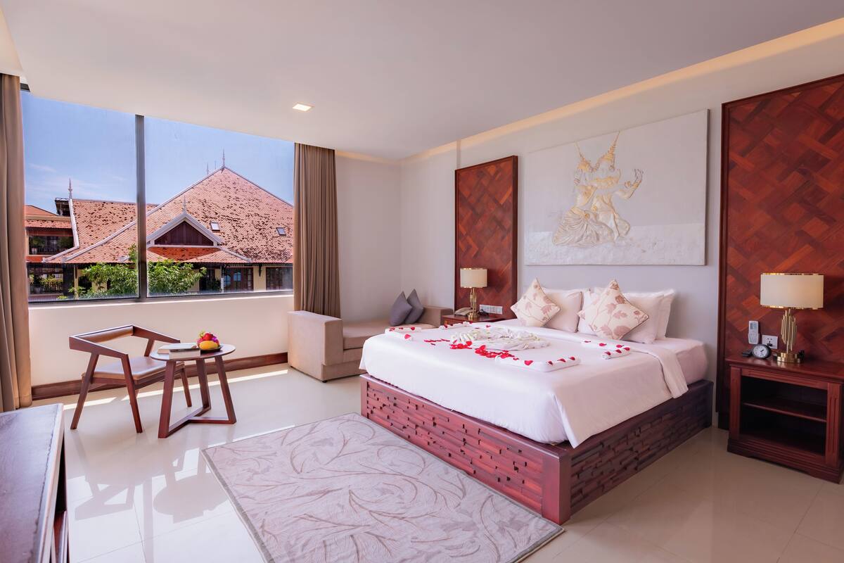 A hotel room with a bed, bedside tables, a desk, and a view of buildings outside.