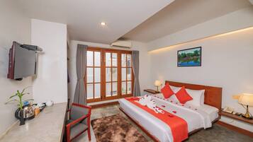 Habitación de hotel con cama, televisión, escritorio, silla, planta y ventana con cortinas.