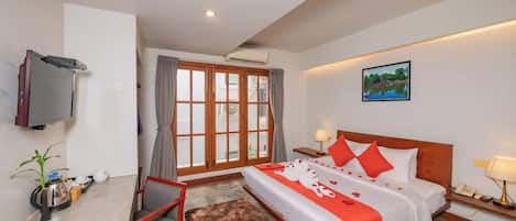 Habitación de hotel con cama, televisión, escritorio, silla, planta y ventana con cortinas.