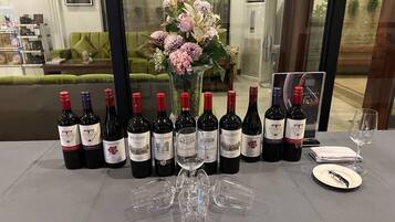 Una mesa con botellas de vino y copas, un florero con flores y un sofá verde al fondo.