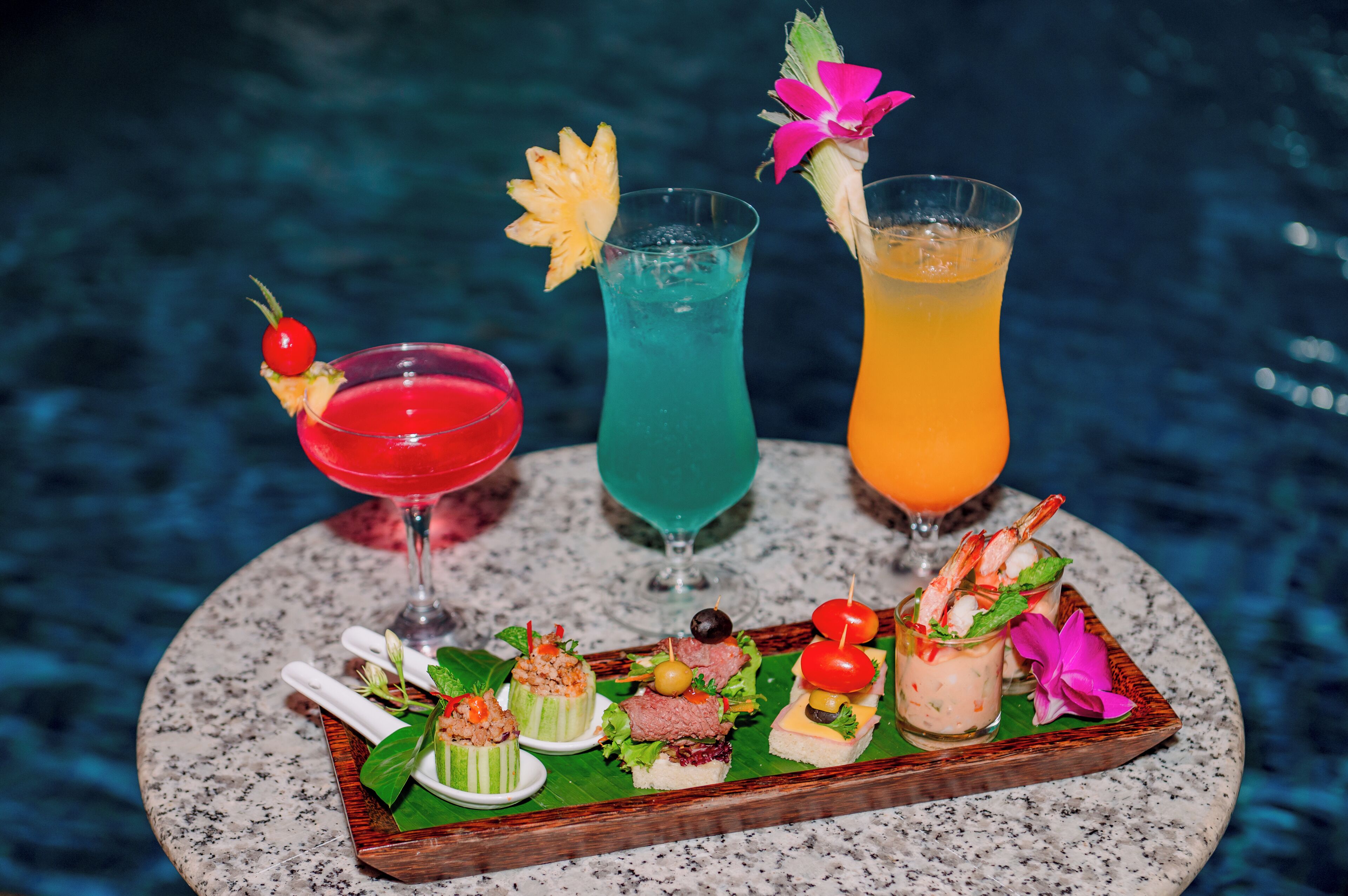 A tray of drinks and appetizers by a poolside.