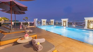 Un espace piscine aménagé sur le toit, avec des chaises longues, des parasols et une vue sur le paysage urbain.