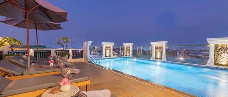 A rooftop pool area with lounge chairs, umbrellas, and a view of the cityscape.