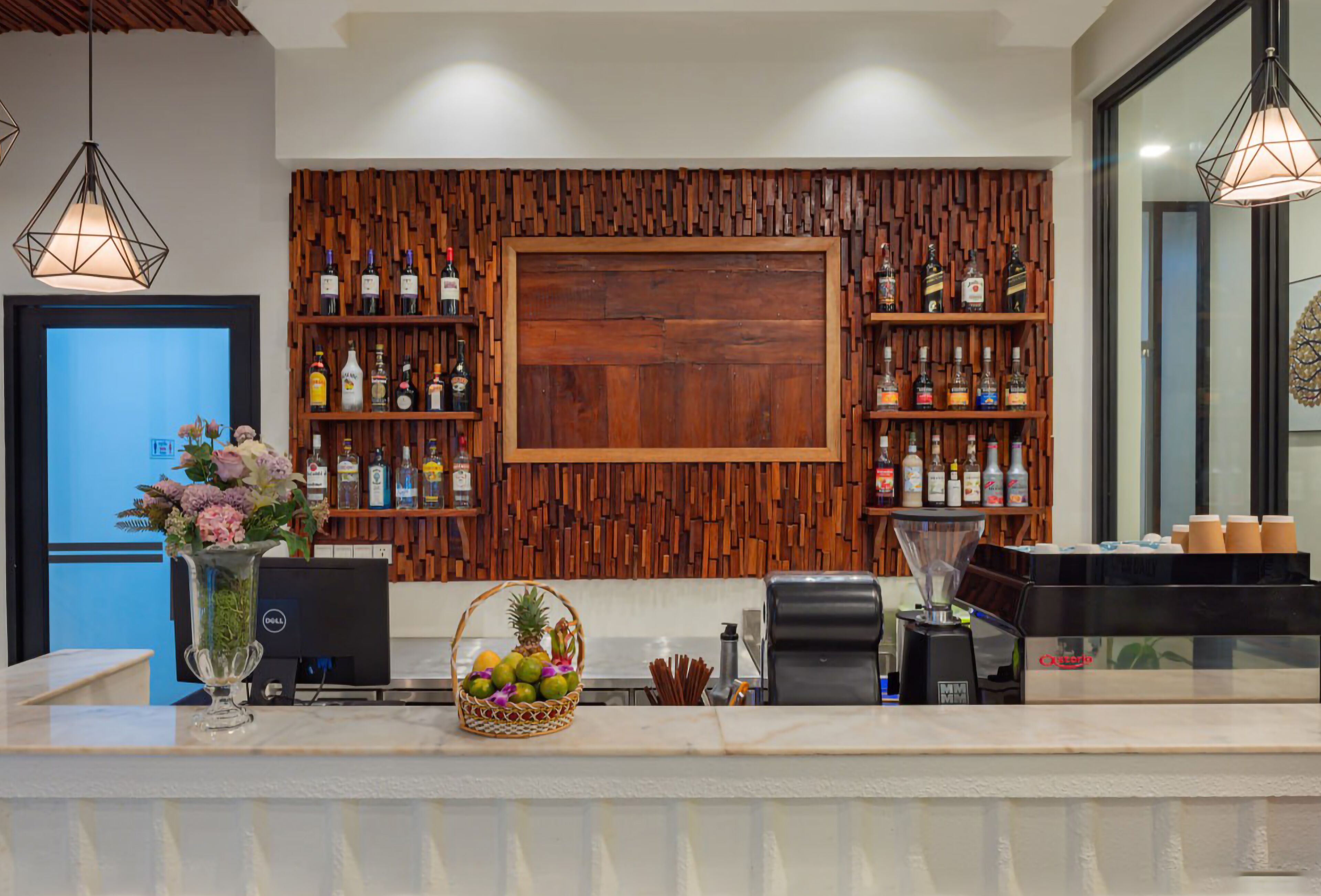 Zona de recepción de un hotel con un panel de pared de madera, una puerta de madera grande y estantes con varias botellas.