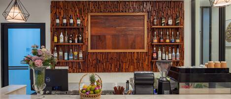 Zona de recepción de un hotel con un panel de pared de madera, una puerta de madera grande y estantes con varias botellas.
