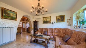 A spacious living room with a large leather sofa, a wooden coffee table, and a chandelier. There are paintings on the walls and a stone archway leading to another room. - Villa Magdalea With Swimming Pool And Seaview (Hlapa (Krk))